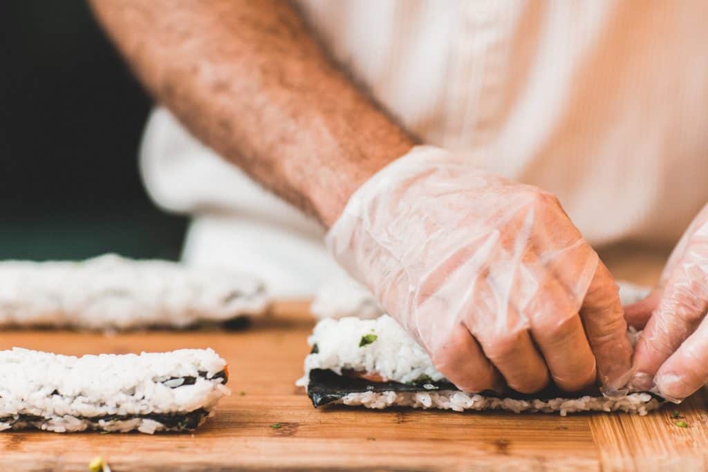 uomo con guanto bianco monouso che prepara il sushi